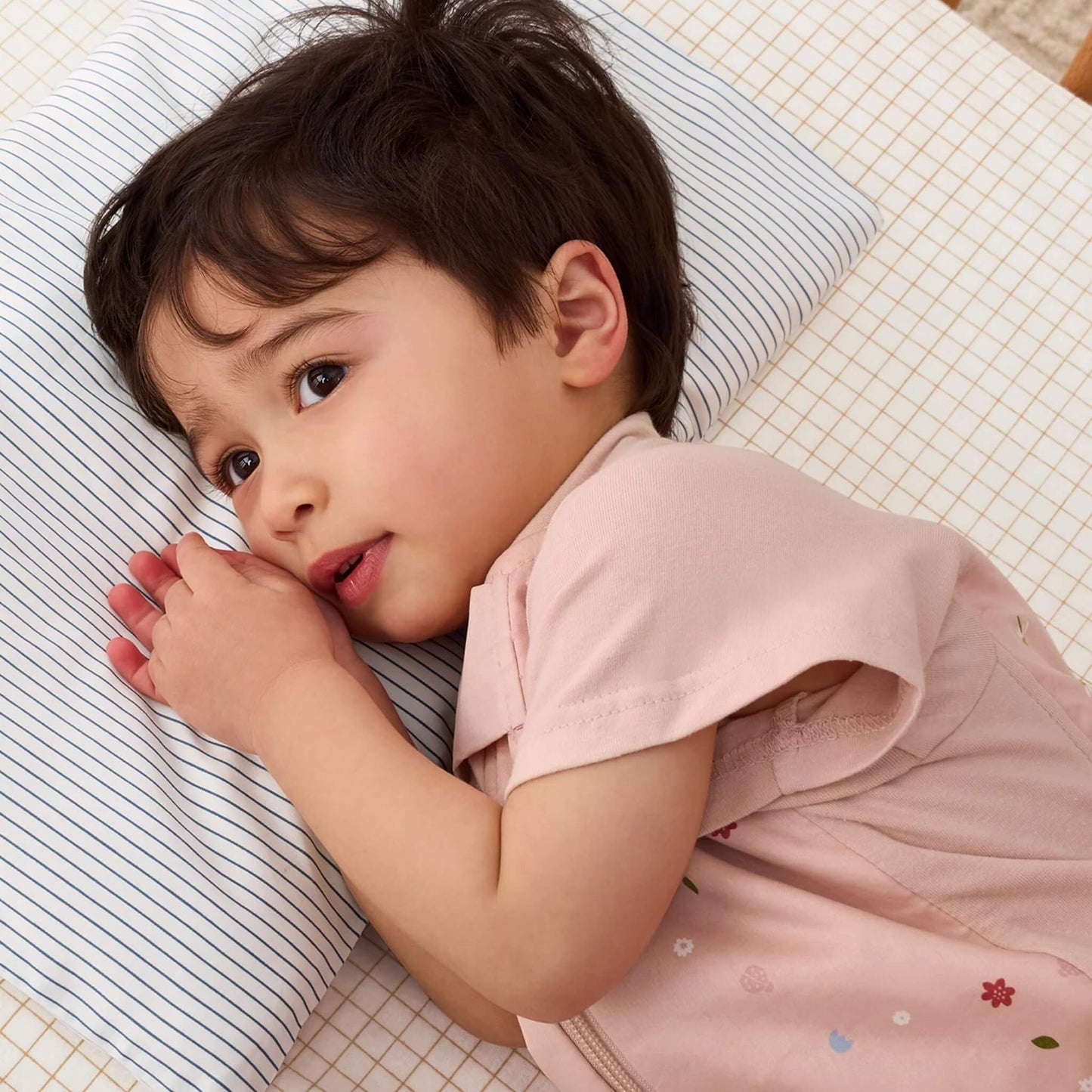 Toddler lying on their side in a cot, resting on a striped white and navy pillow with a soft expression.