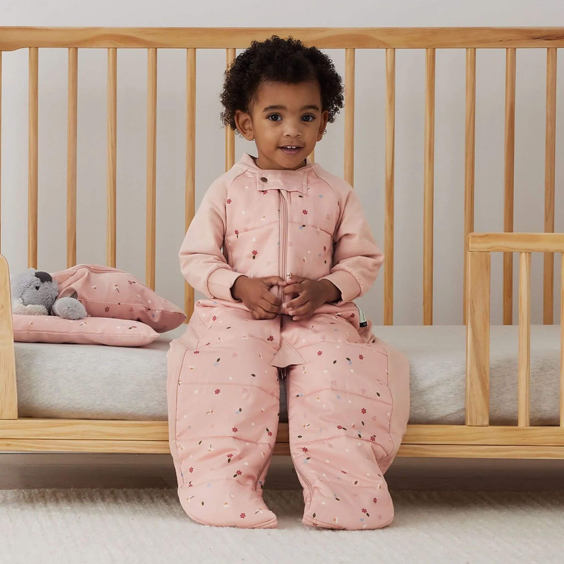 Close up of pink organic cotton fabric patterned with small white daisies, ladybirds and scattered green leaves.