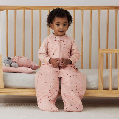 Close up of pink organic cotton fabric patterned with small white daisies, ladybirds and scattered green leaves.