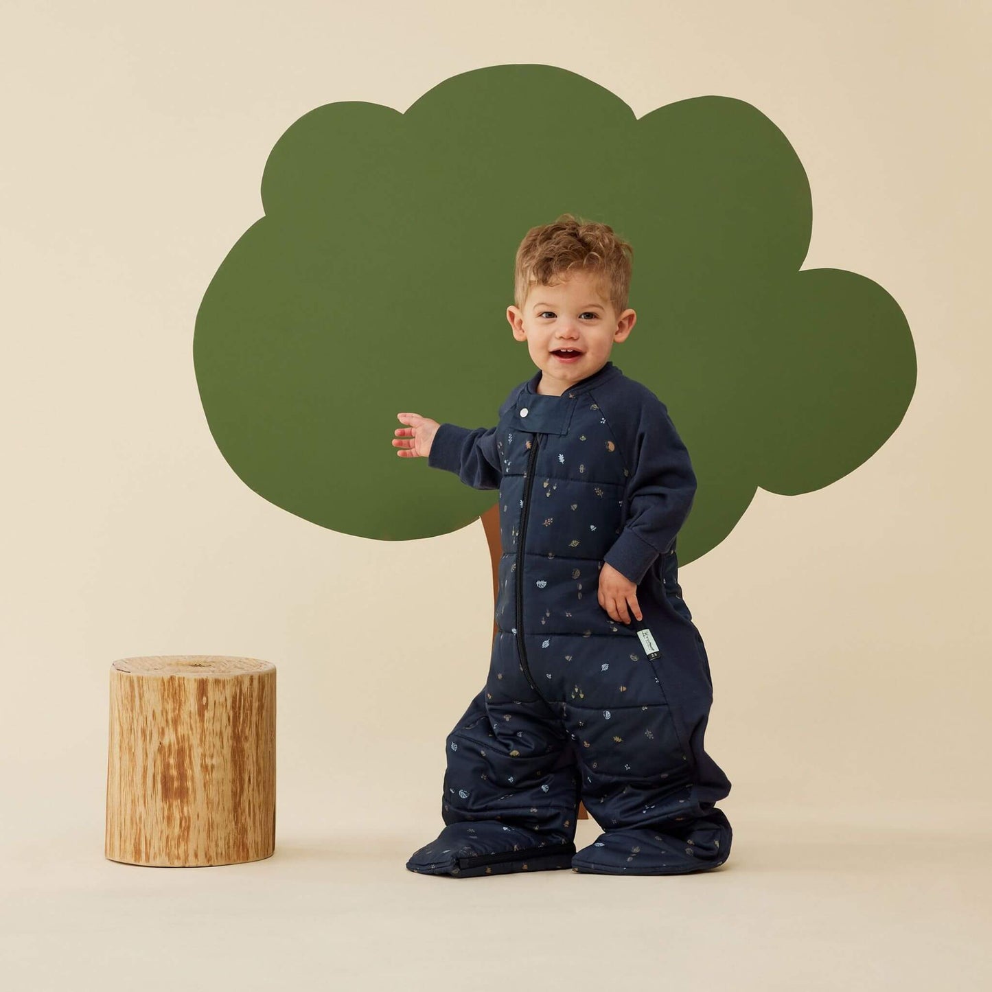 Smiling toddler wearing a sleep suit bag in navy with hedgehog print, standing in sleep suit mode with legs separated.