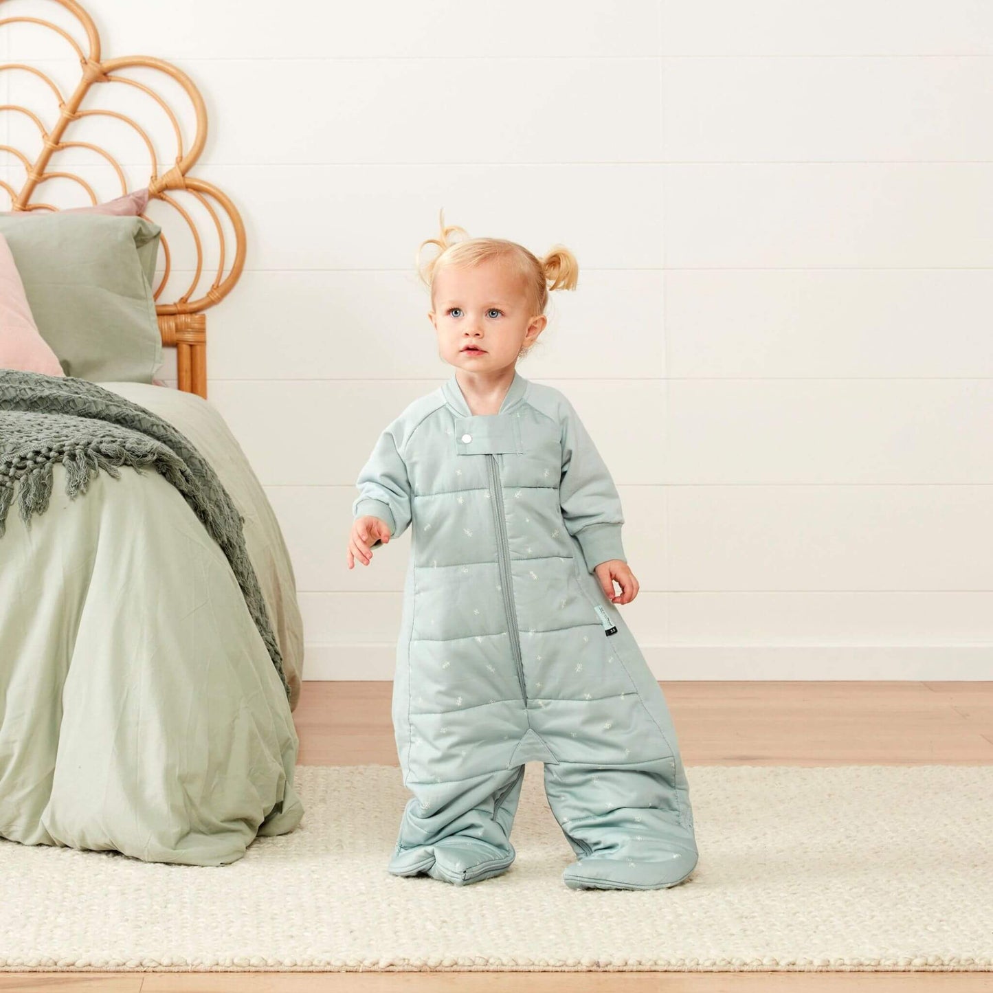 Toddler standing in a sage padded sleep suit bag with legs separated into suit mode.