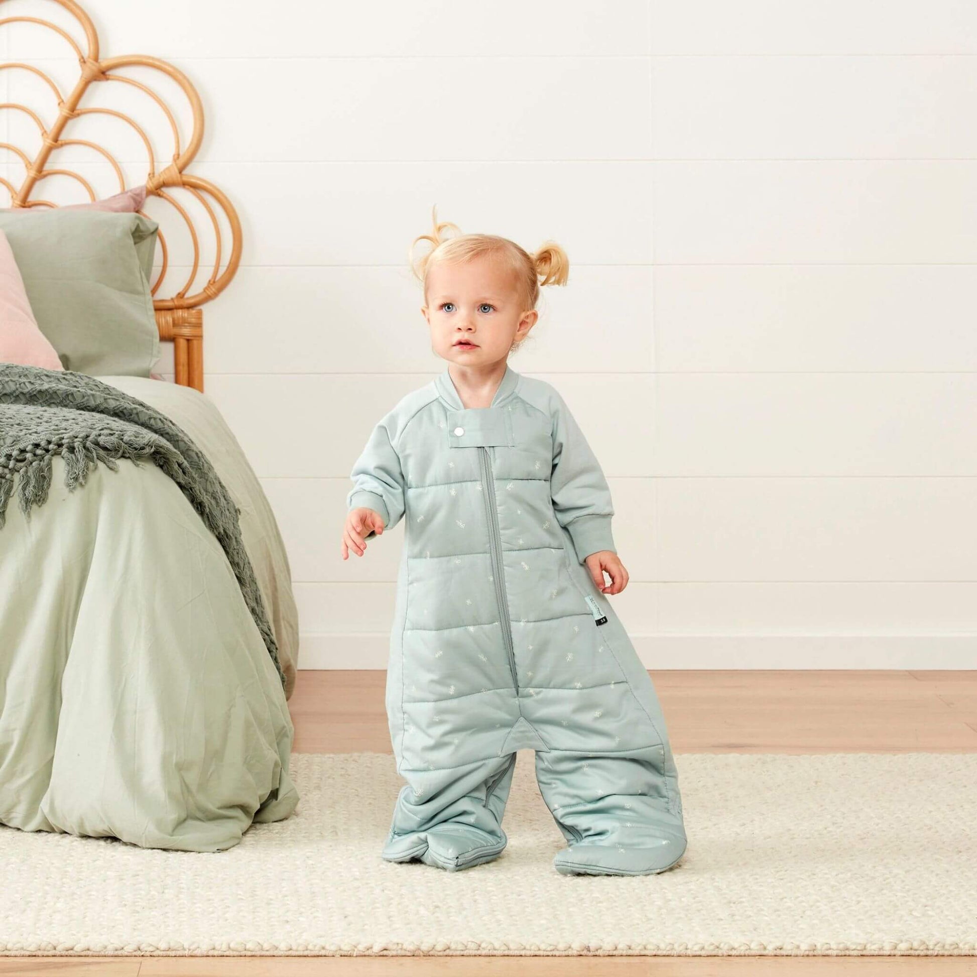 Toddler standing in a sage padded sleep suit bag with legs separated into suit mode.