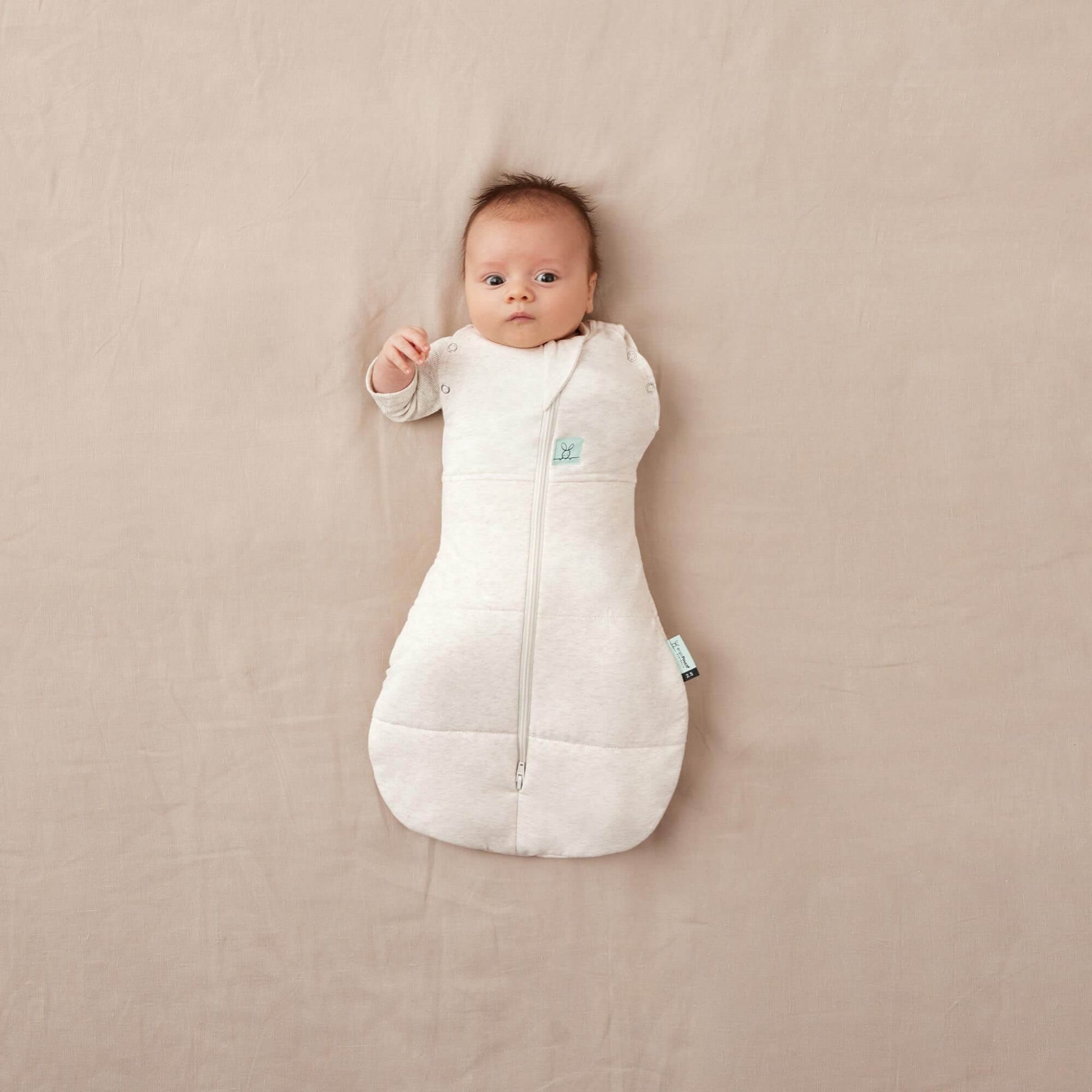 Baby in winter weight TOG cocoon swaddle bag, oatmeal colour, arm partially unswaddled, organic and breathable fabric for cosy winter warmth.
