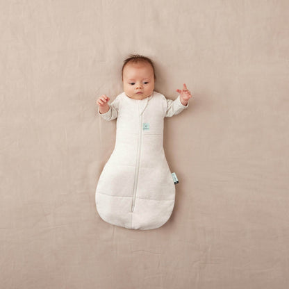 Baby in a cocoon swaddle bag, oatmeal colour, arms fully unswaddled.