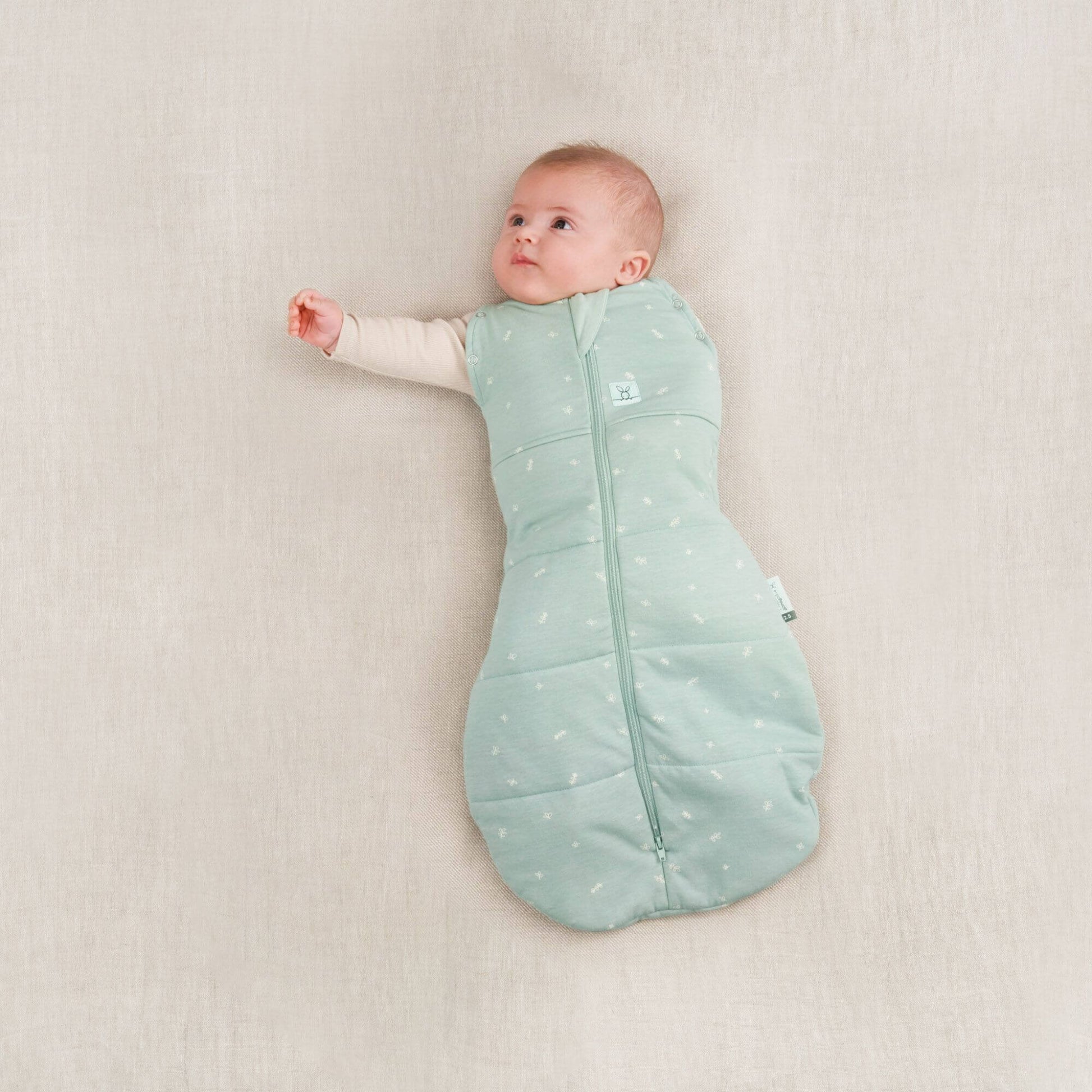 Baby in a winter weight 2.5 TOG swaddle bag, sage colour, with one arm out and one arm swaddled.