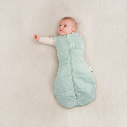 Baby in a winter weight 2.5 TOG swaddle bag, sage colour, with one arm out and one arm swaddled.
