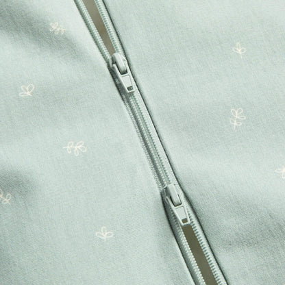 Close-up of a sage green baby Swaddle Bag showing a two-way zip detail with small white motifs on the fabric.