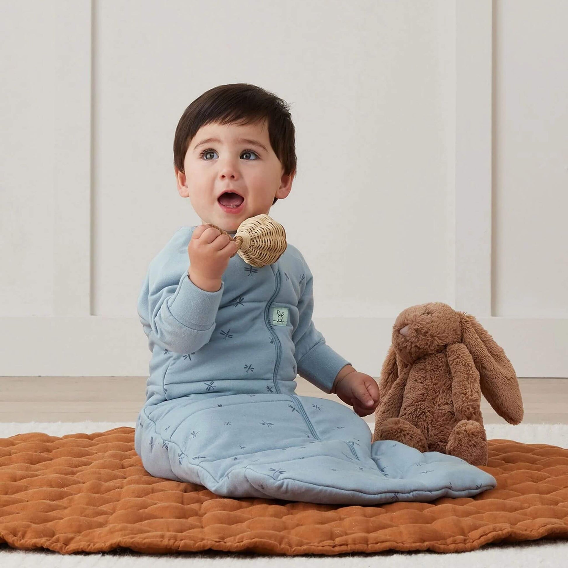 Toddler sitting comfortably in a winter weight sleeping bag in Dragonflies print, playing on a soft quilted mat.