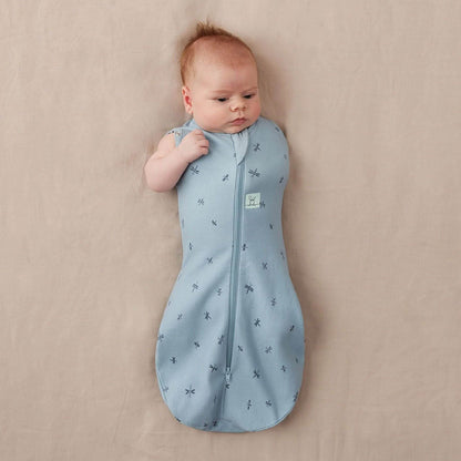 A baby wearing a Swaddle Bag in dragonflies print, transitioning with arm-out option for added comfort and mobility.