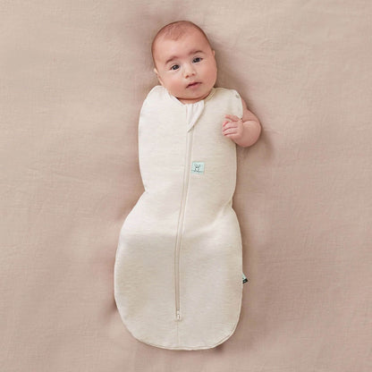 Baby comfortably resting in Cocoon Swaddle Bag in oatmeal, showcasing its arm-out option for flexible and safe sleeping.
