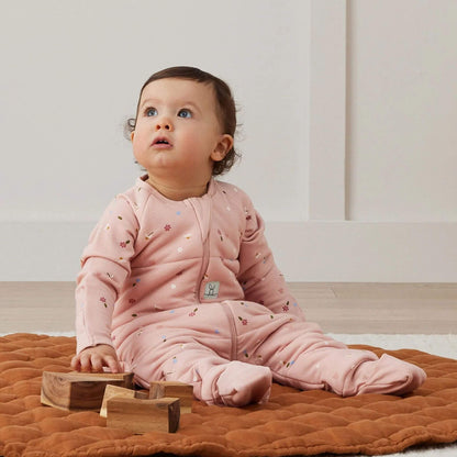 Baby seated and wearing a winter weight Sleep Onesie. The Onesie features a soft pink fabric with delicate floral print, providing both comfort and style for sleep or play.