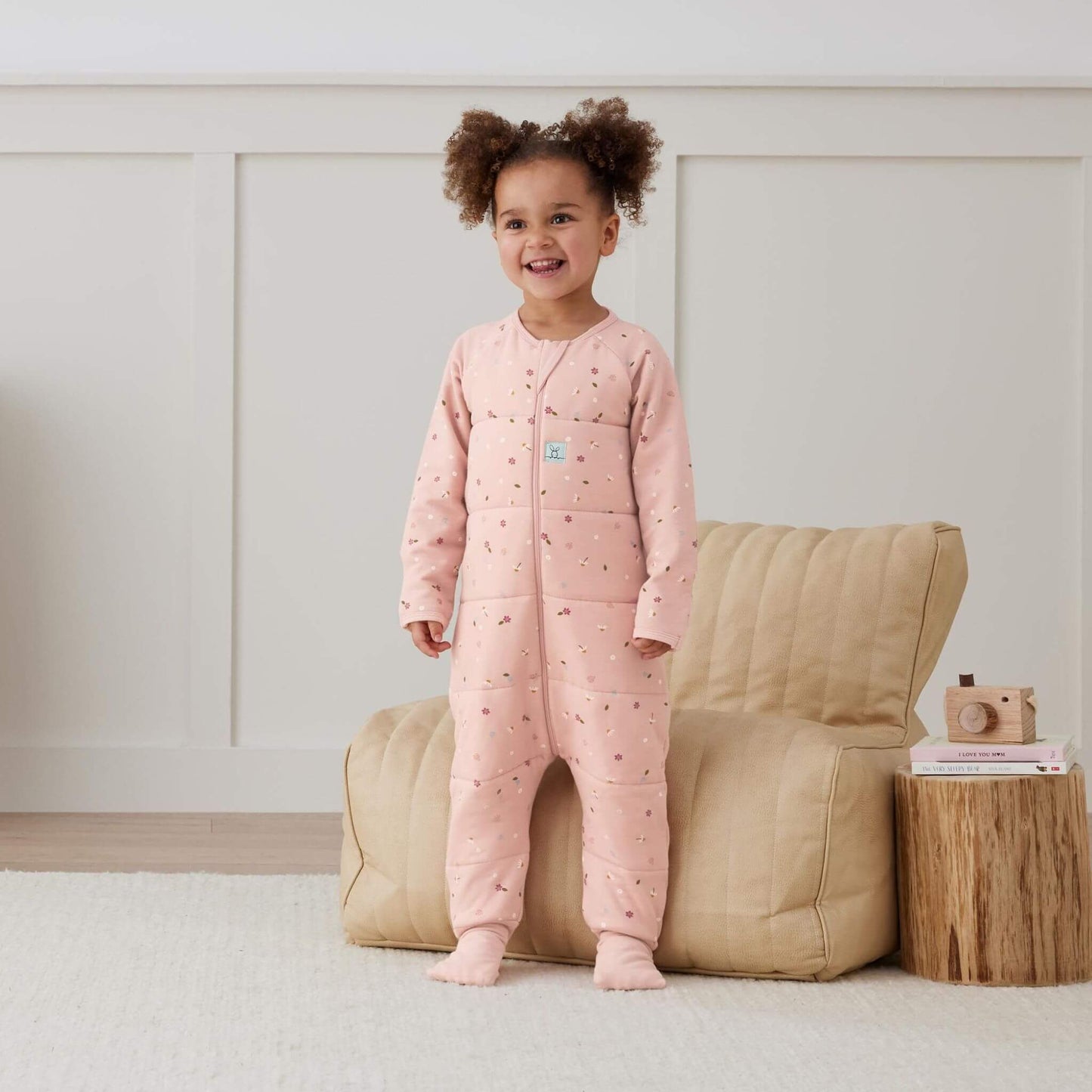 Smiling toddler models a winter weight Sleep Onesie. The Onesie features a pink design with delicate floral accents, offering a cosy and breathable fit for sleep.