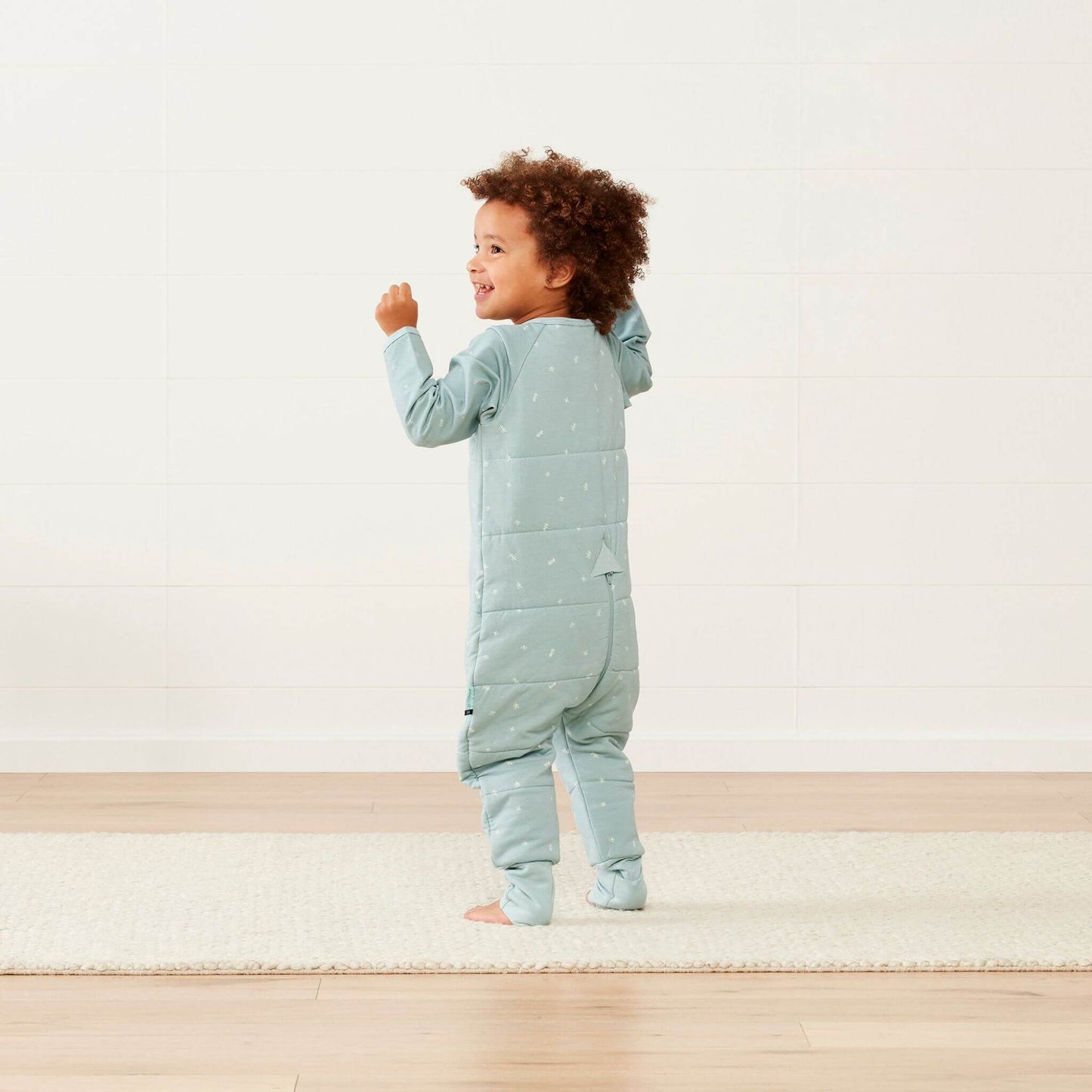 Toddler wearing a winter weight Sleep Onesie in sage green, showcasing the cosy quilted back and flexible fabric for comfortable movement.