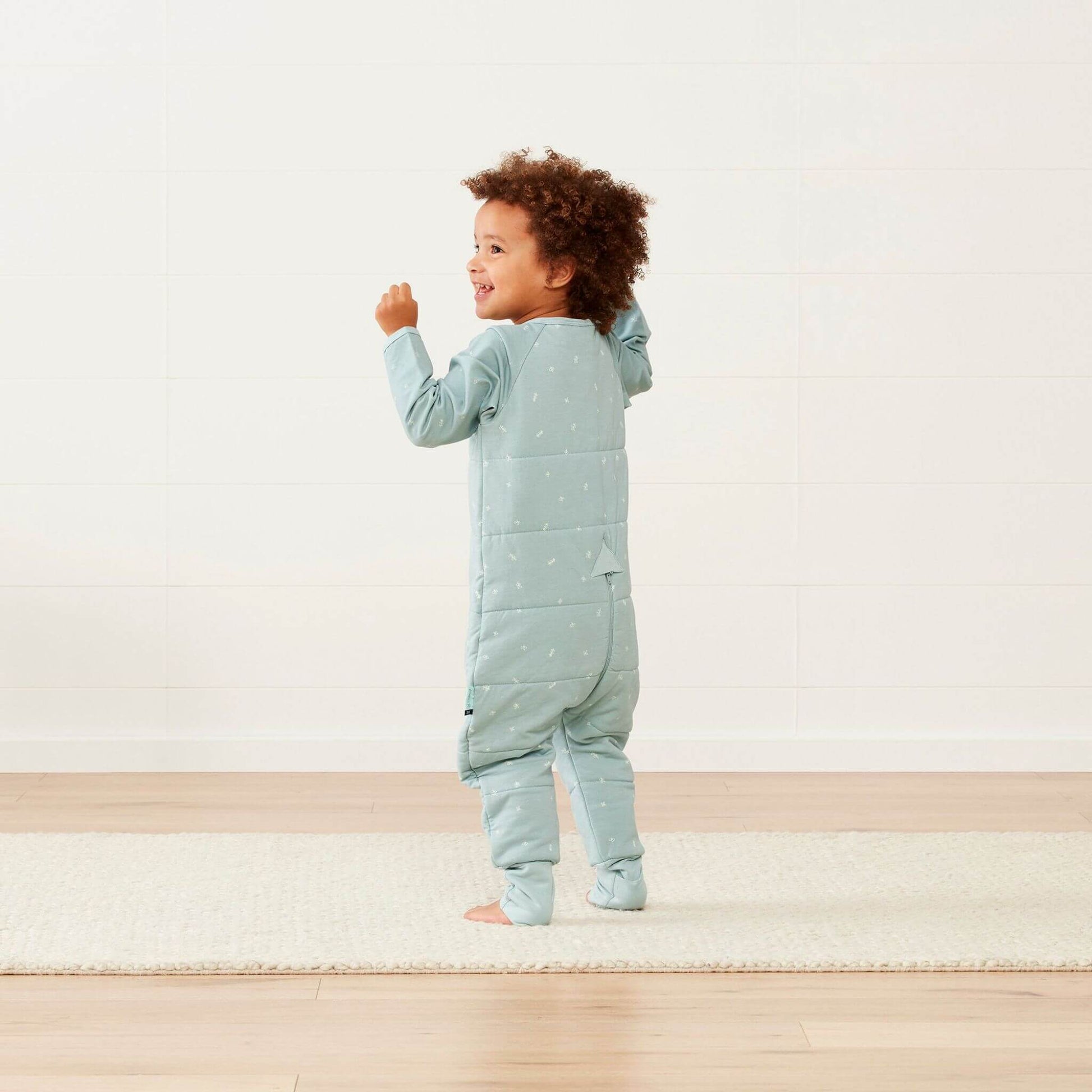 Toddler wearing a winter weight Sleep Onesie in sage green, showcasing the cosy quilted back and flexible fabric for comfortable movement.