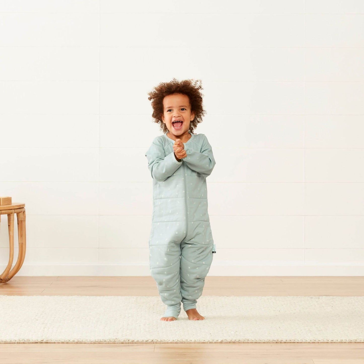 Toddler laughing and clapping while a Sleep Onesie in sage green, highlighting its snug fit and playful design.