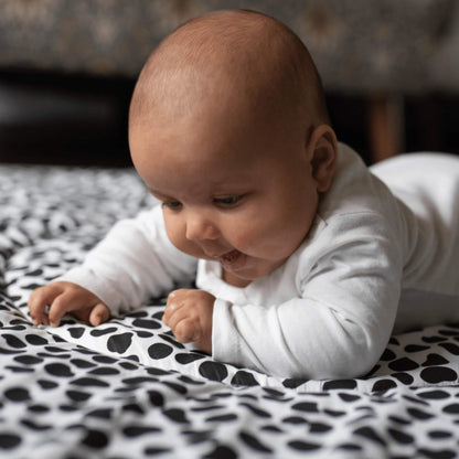 Baby lying on tummy on a padded black and white patterned playmat, focusing closely on the bold high contrast shapes during floor play.
