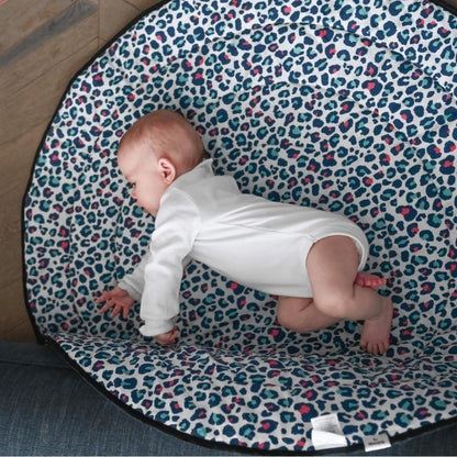 Baby practising tummy time on a soft padded mat with blue and pink leopard print pattern, positioned on a wooden floor.