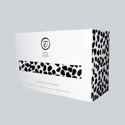 White product box with black spot print sides and logo branding, packaging for a reversible sensory playmat.