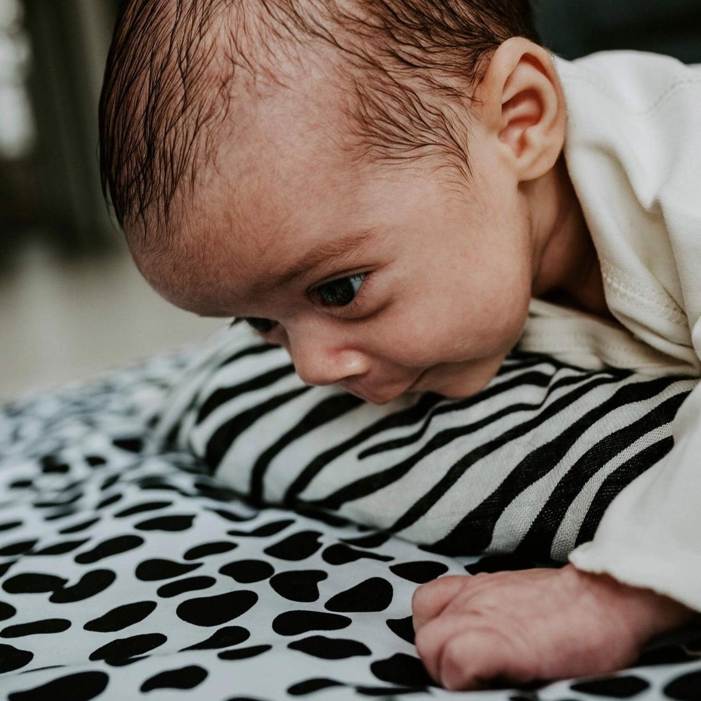 Close up of a baby’s face and hands resting on a black and white striped and spotted high contrast surface during tummy time.