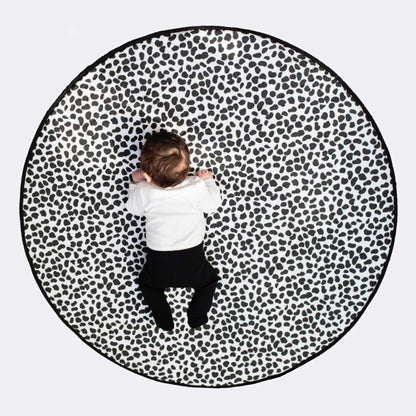 Overhead view of a baby centred on a large round black and white patterned mat, highlighting full coverage size and bold visual design.