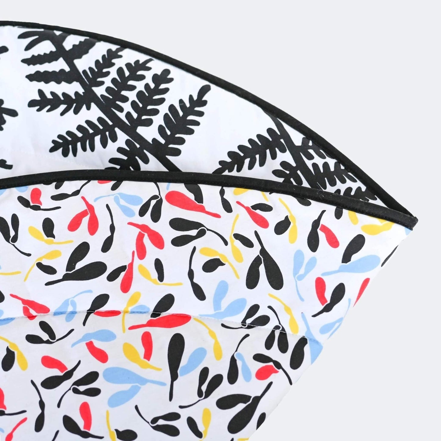 Close-up of folded playmat corner showing reversible design with black botanical print and colourful developmental pattern.