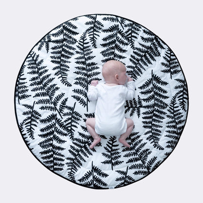Overhead view of baby lying centred on large round cushioned playmat with bold black botanical print for tummy time.