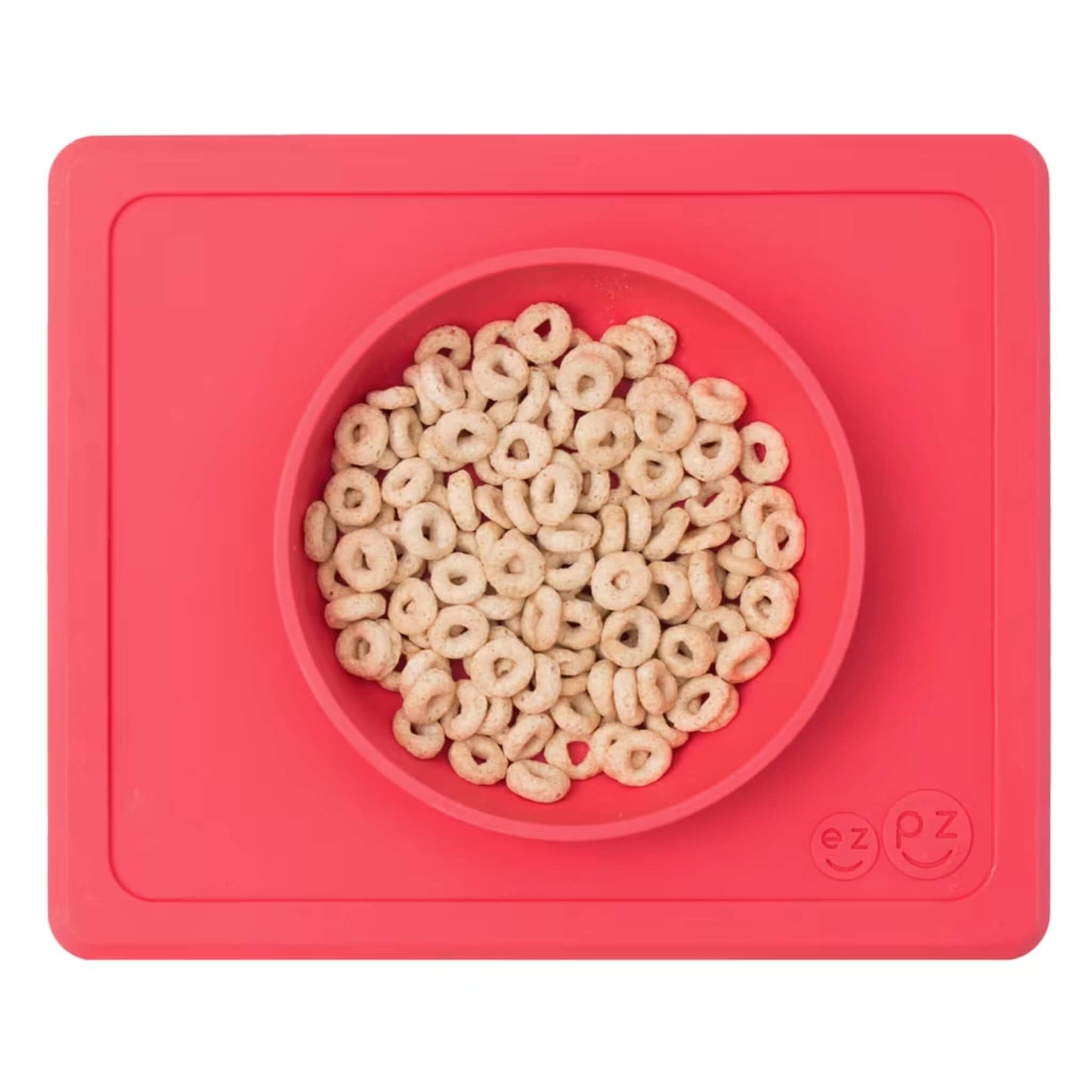 Coral silicone suction bowl with built-in placemat, filled with cereal hoops, shown from above.