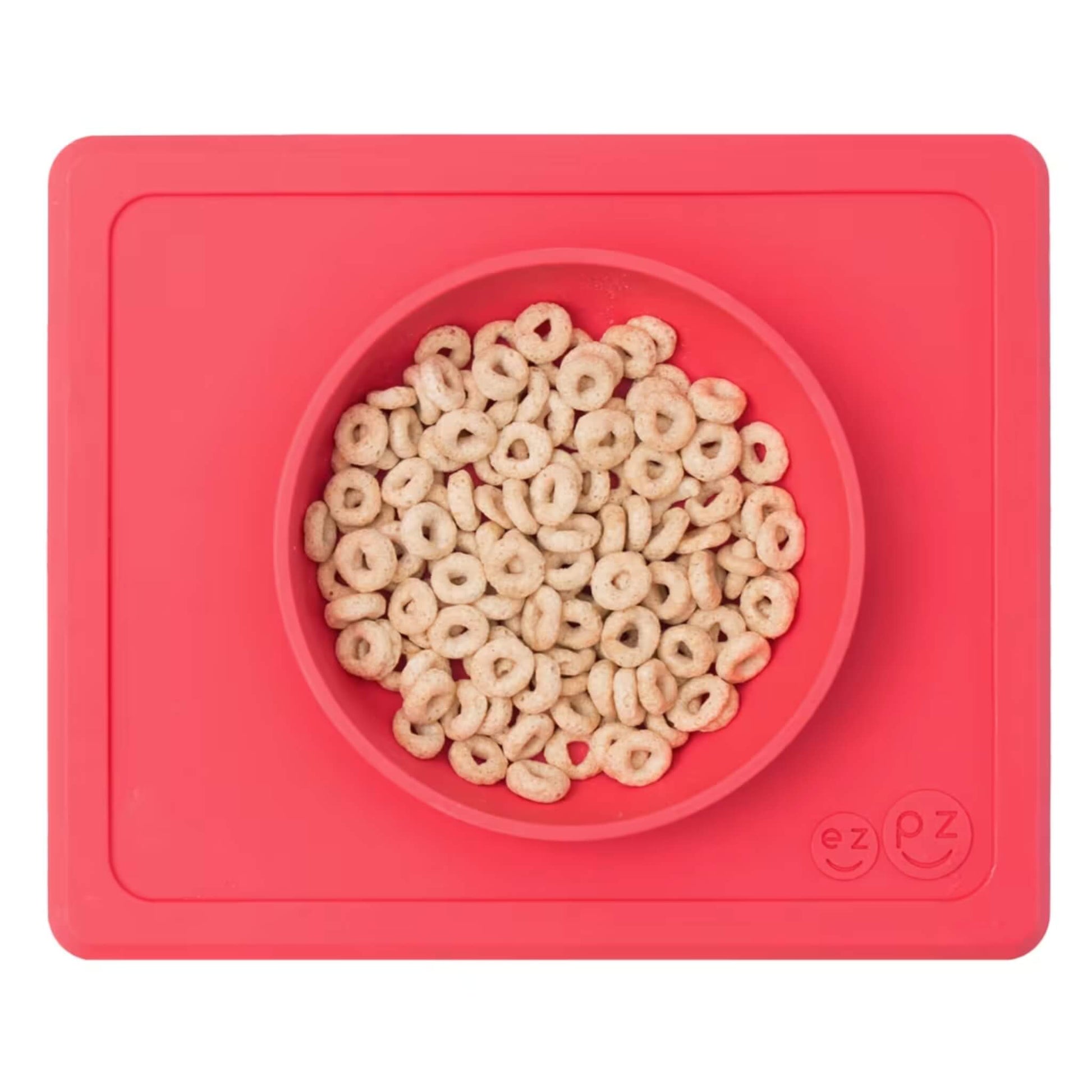 Coral silicone suction bowl with built-in placemat, filled with cereal hoops, shown from above.