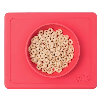 Coral silicone suction bowl with built-in placemat, filled with cereal hoops, shown from above.