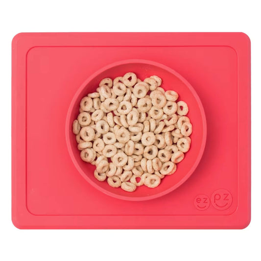 Coral silicone suction bowl with built-in placemat, filled with cereal hoops, shown from above.