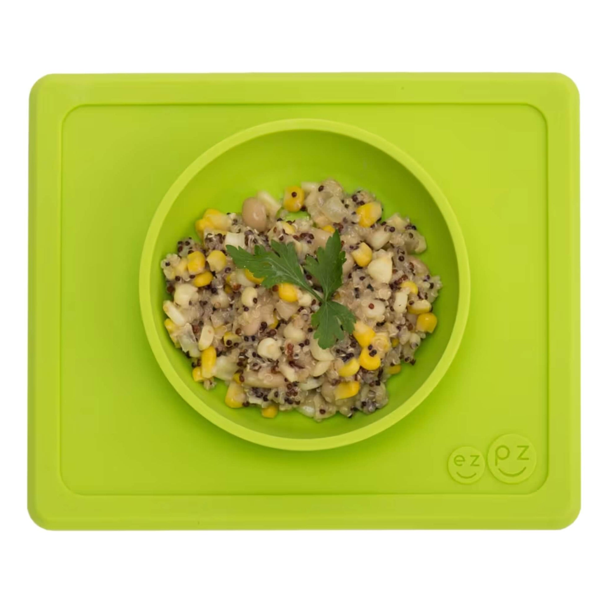 Lime silicone suction bowl with built-in placemat, filled with quinoa, sweetcorn and herbs, shown from above.