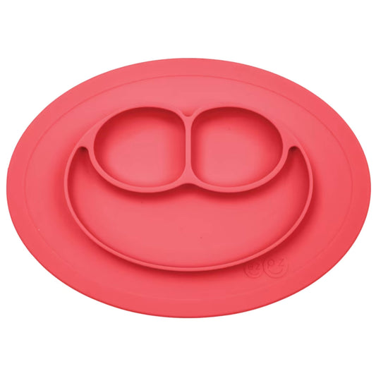 Ezpz Mini Mat in coral silicone, an all-in-one suction placemat and baby plate with three divided sections arranged in a smile design