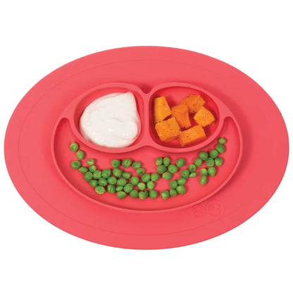 Coral silicone suction placemat with three divided sections containing  food including peas, sweet potato and yoghurt.