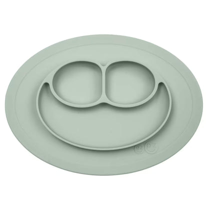 Ezpz Mini Mat in sage green silicone, an all-in-one suction placemat and baby plate with three divided sections arranged in a smile design.