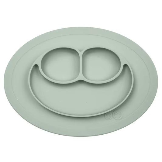 Ezpz Mini Mat in sage green silicone, an all-in-one suction placemat and baby plate with three divided sections arranged in a smile design.