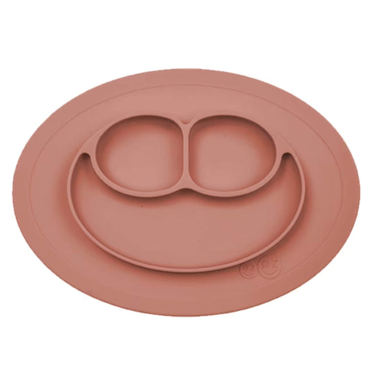 Ezpz Mini Mat in sienna silicone, an all-in-one suction placemat and toddler plate with three divided sections shaped like a smiley face.