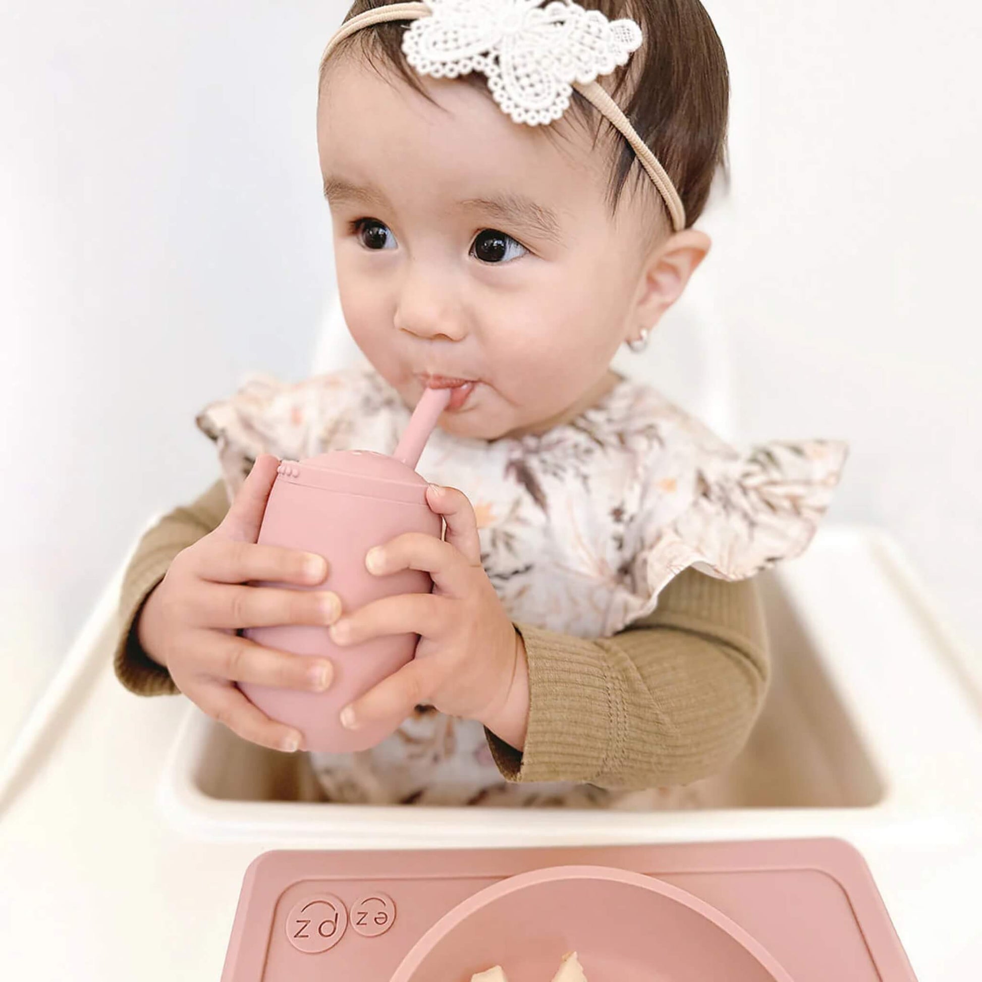 Toddler drinking from a pink straw cup while seated in highchair, demonstrating independent drinking skills