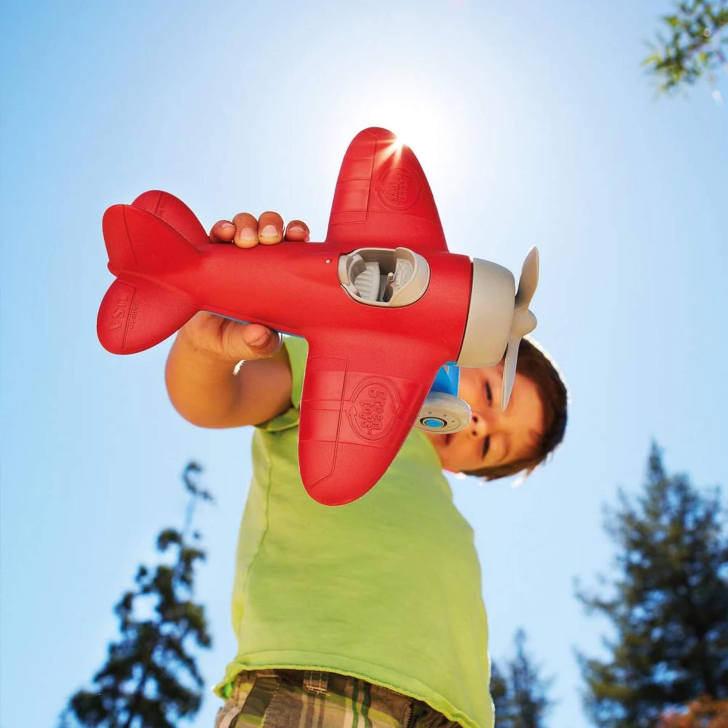 Young child holding the red toy airplane outdoors, with the wingspan clearly visible against a bright blue sky.