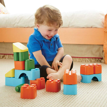 Toddler laughing while playing with oversized building blocks arranged in towers on the floor.