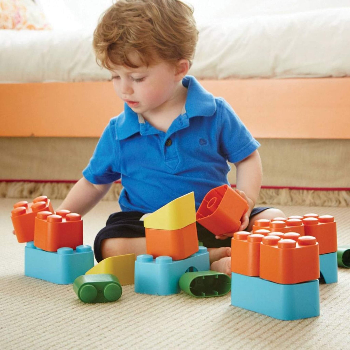 Child carefully exploring and stacking chunky building blocks in various colours on a carpeted floor.