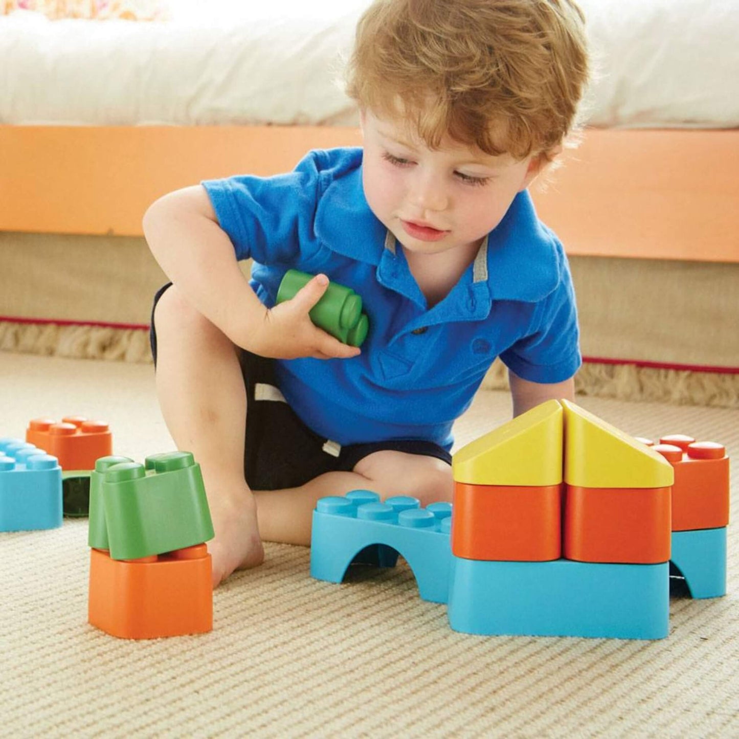 Close-up of a toddler building with blue, orange, green and yellow blocks, focused on creating shapes and structures.