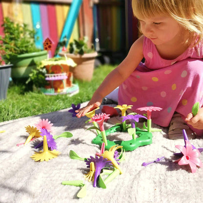 Child in a pink dress playing with the Build-a-Bouquet set outside, placing flower pieces into the base while surrounded by colourful parts.
