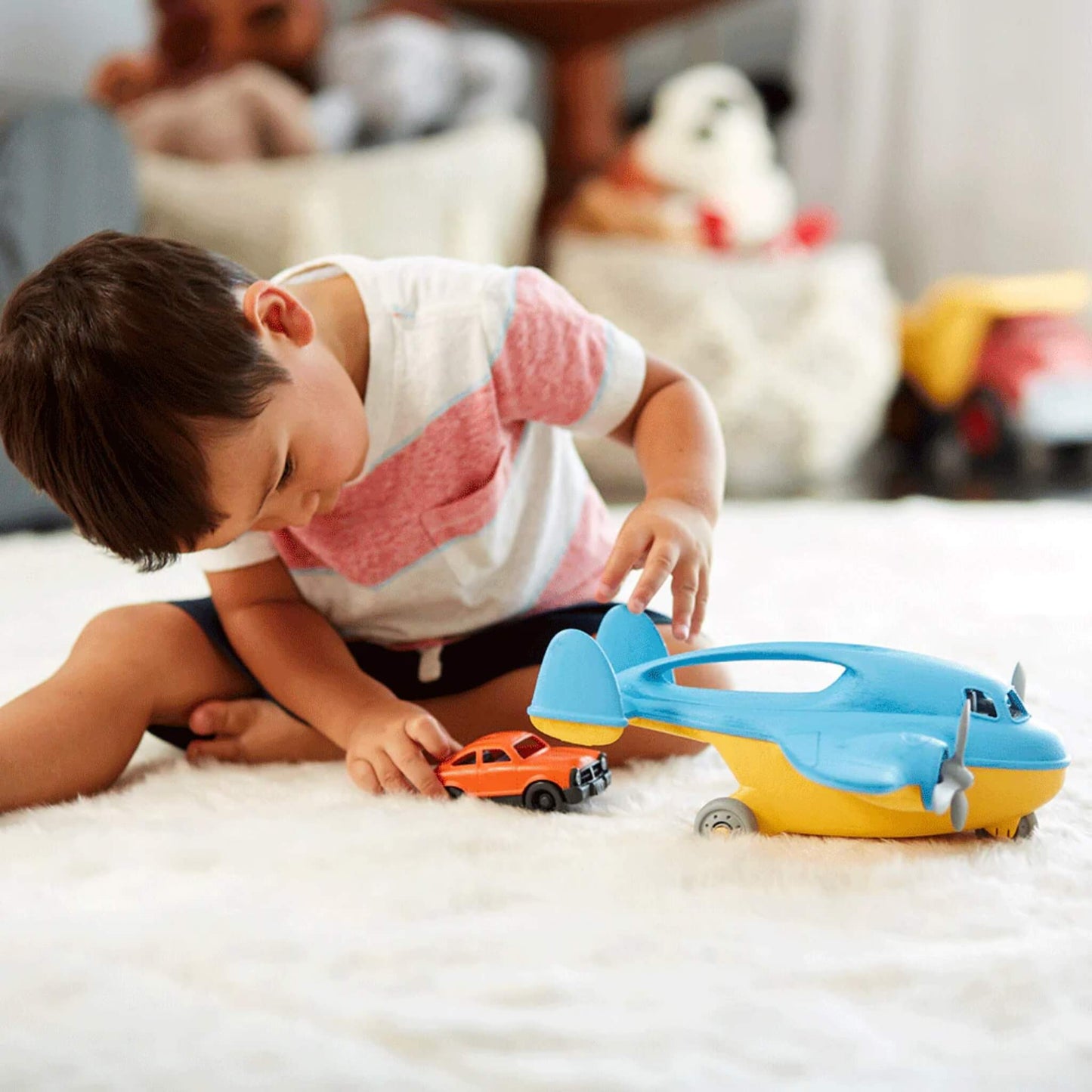 A young child playing on the floor, unloading the orange mini car from the open cargo hold of the toy plane.