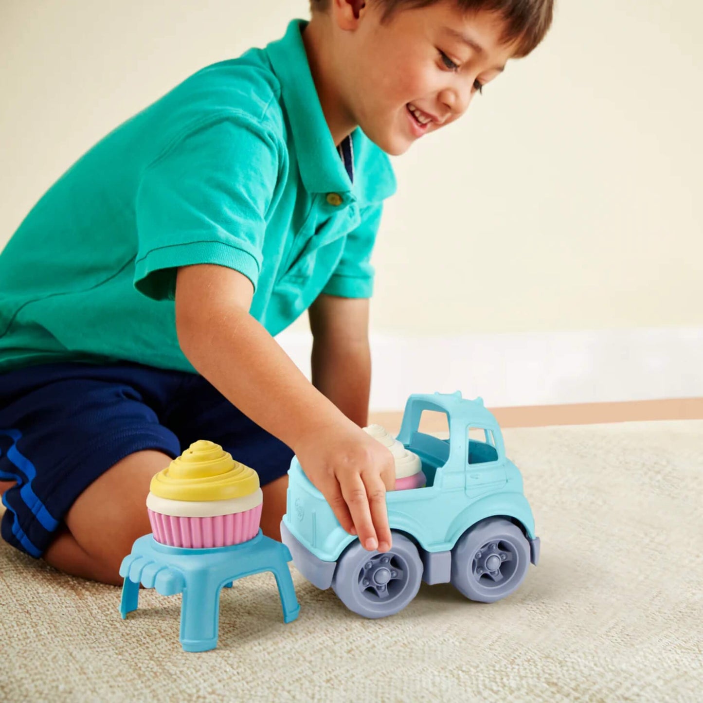 A young boy smiling as he places a cupcake on the included stand beside the Cupcake Truck.