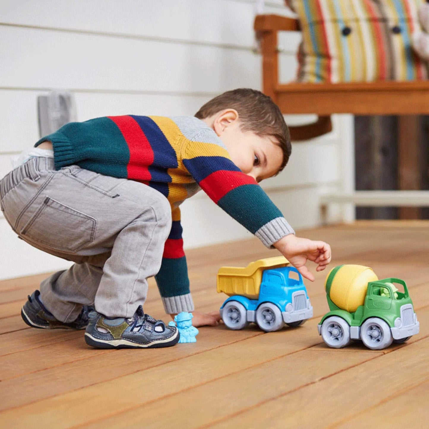 Young child playing on a wooden floor with the Dumper truck and cement mixer, engaging in imaginative vehicle play.