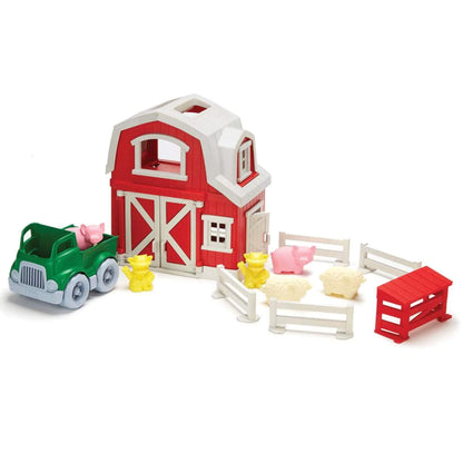 Green Toys Farm Set shown fully assembled with red and white barn, green pickup truck, yellow farmer figures, pigs, sheep, fences, and a small red hog shed.
