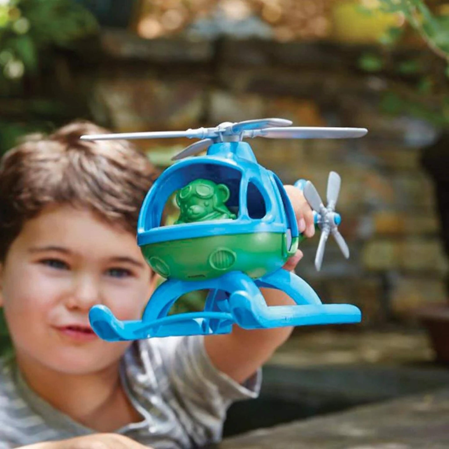 Child holding the toy helicopter mid-air outdoors, with the bear pilot figure clearly visible through the cockpit window.