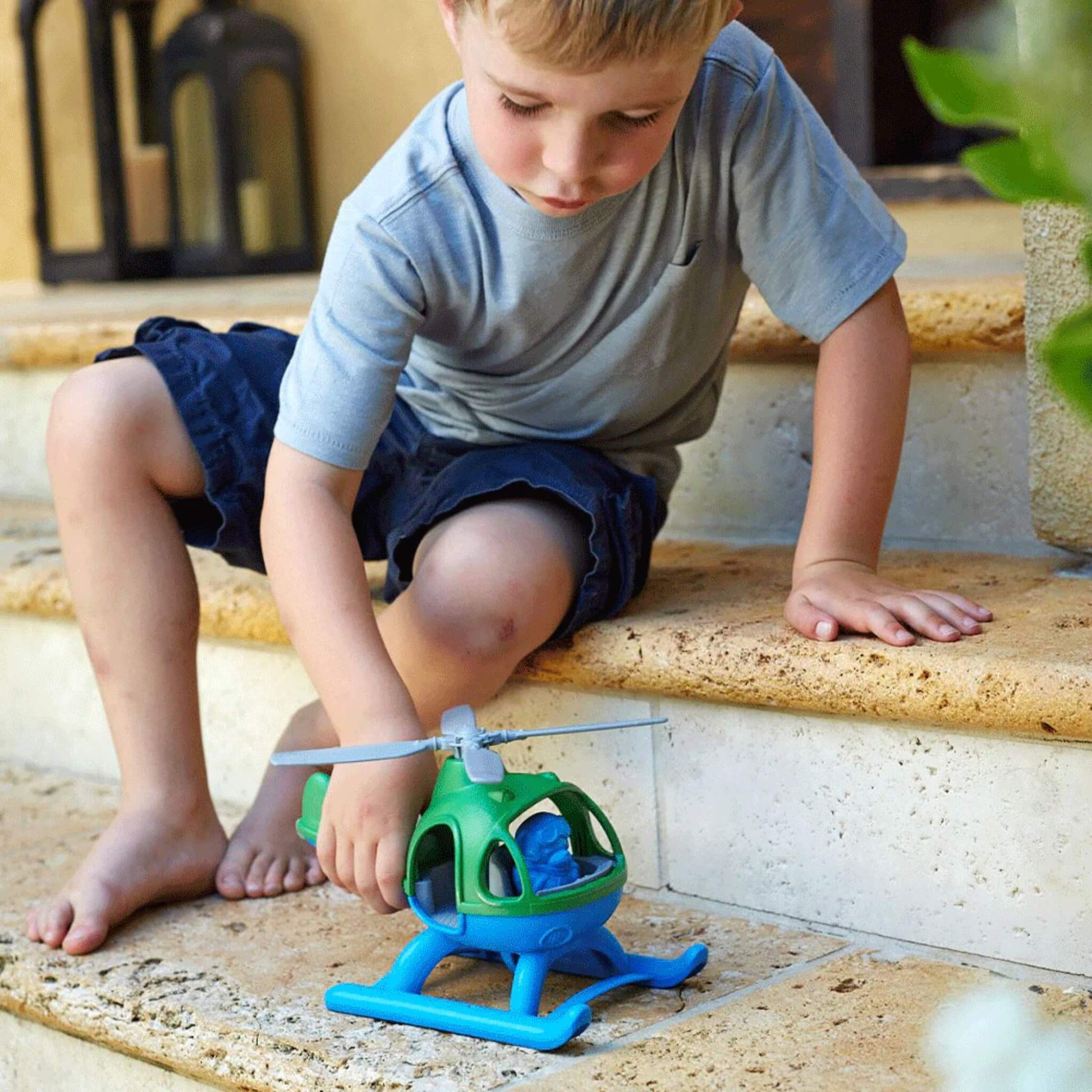 Young child sitting on stone steps, rolling the toy helicopter along the step surface during play.