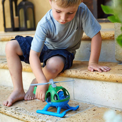 Young child sitting on stone steps, rolling the toy helicopter along the step surface during play.
