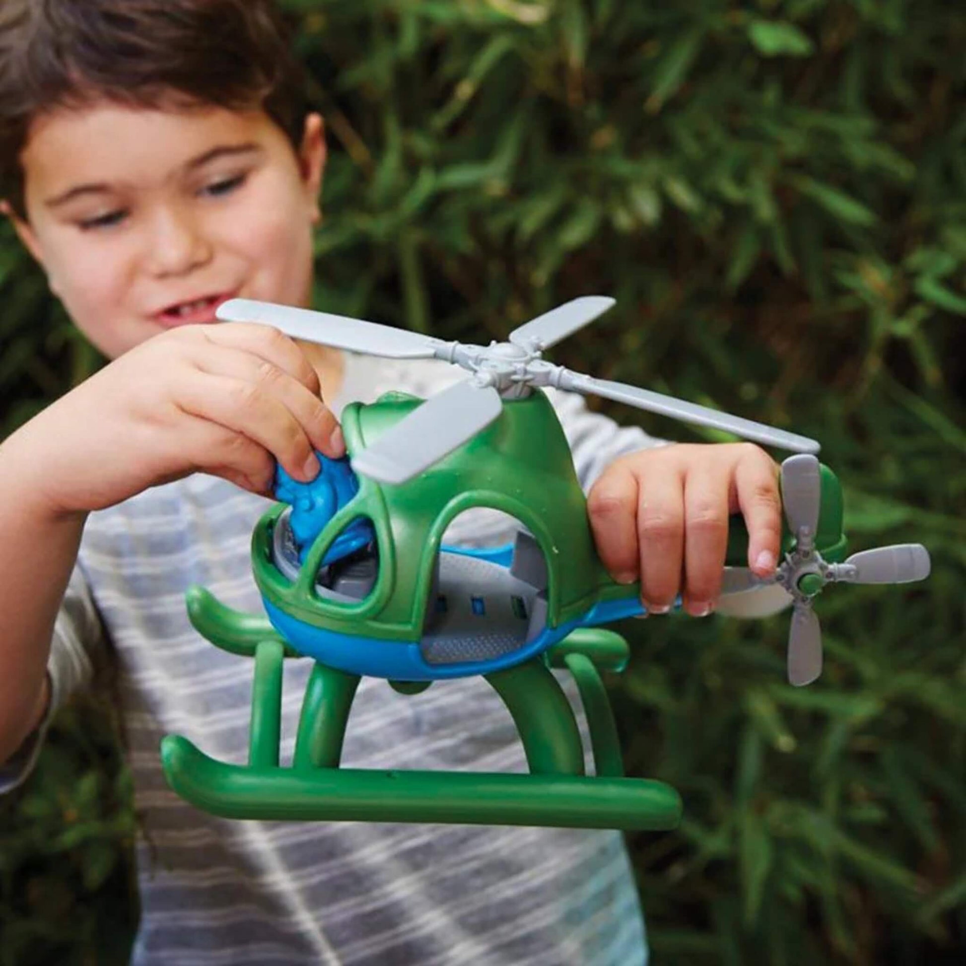 Child playing outdoors, inserting the blue pilot figure into the cockpit of the green and blue toy helicopter.